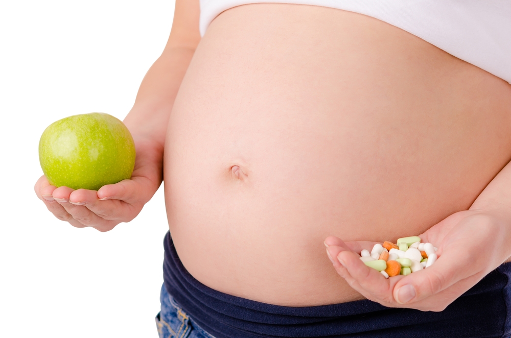 Pregnant holding apple and vitamins